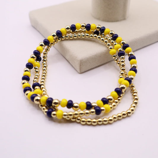 Three Gold bracelet with blue and yellow beads on a white surface
