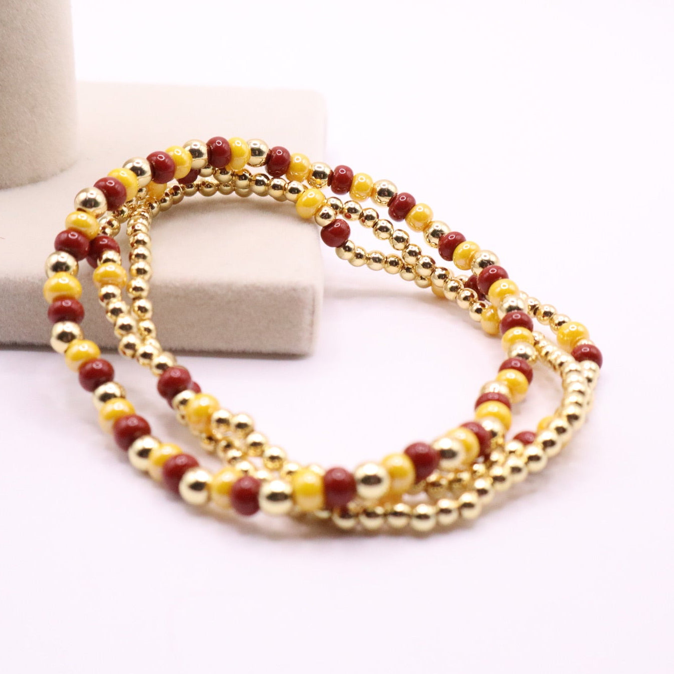 Multistrand beaded bracelet with gold and burgundy beads on a white surface