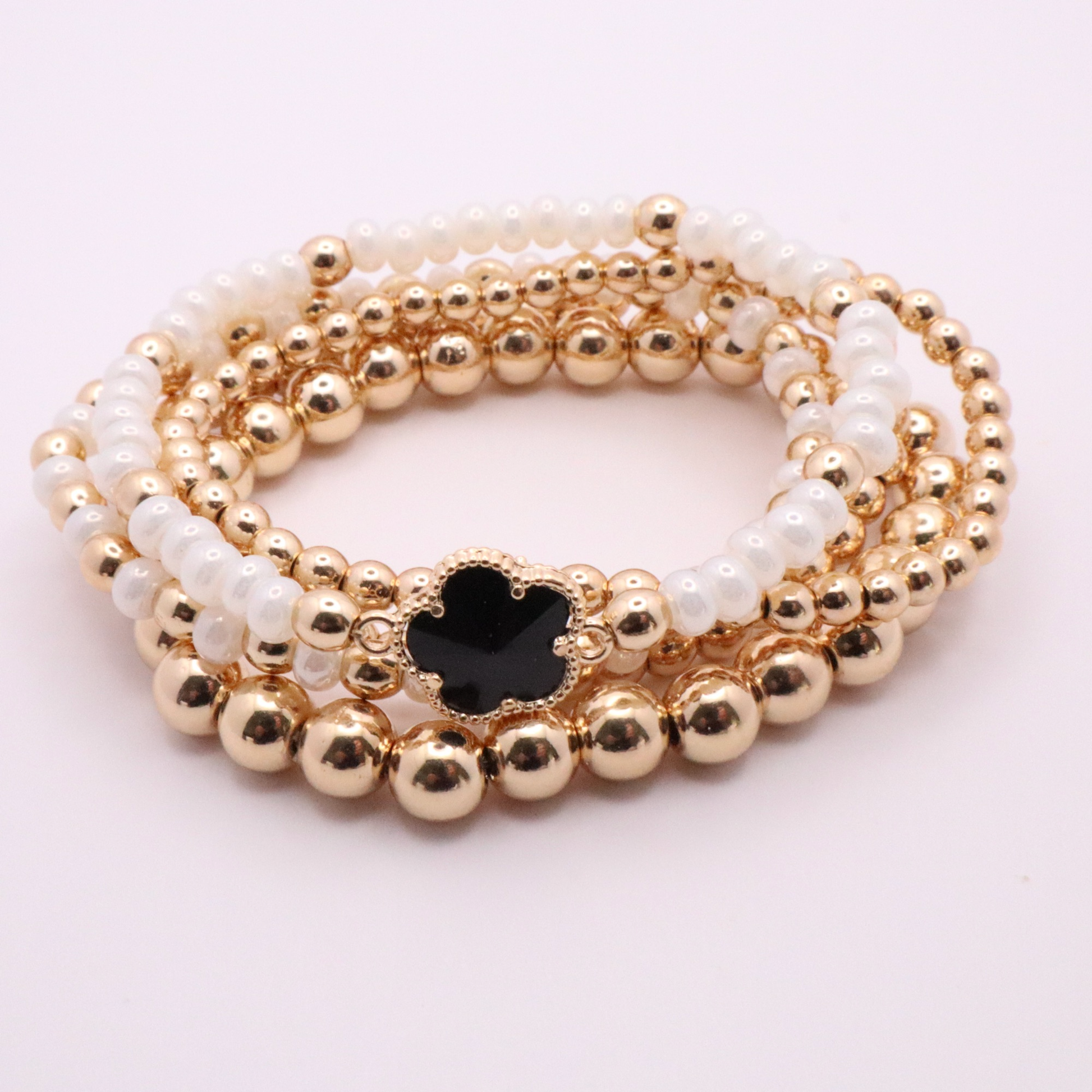 Set of 5 of gold toned beaded bracelets with white seed beads and hematite gold accents. One bracelet features a black clover charm. The bracelets are displayed on a white background.