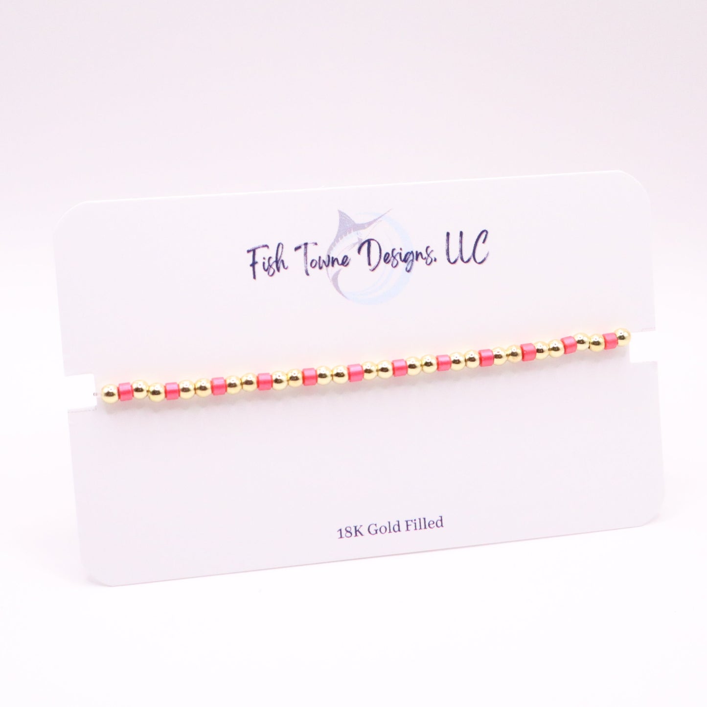 Gold and pink beaded bracelet on a white card with 'Fish Towne Designs, LLC' branding.