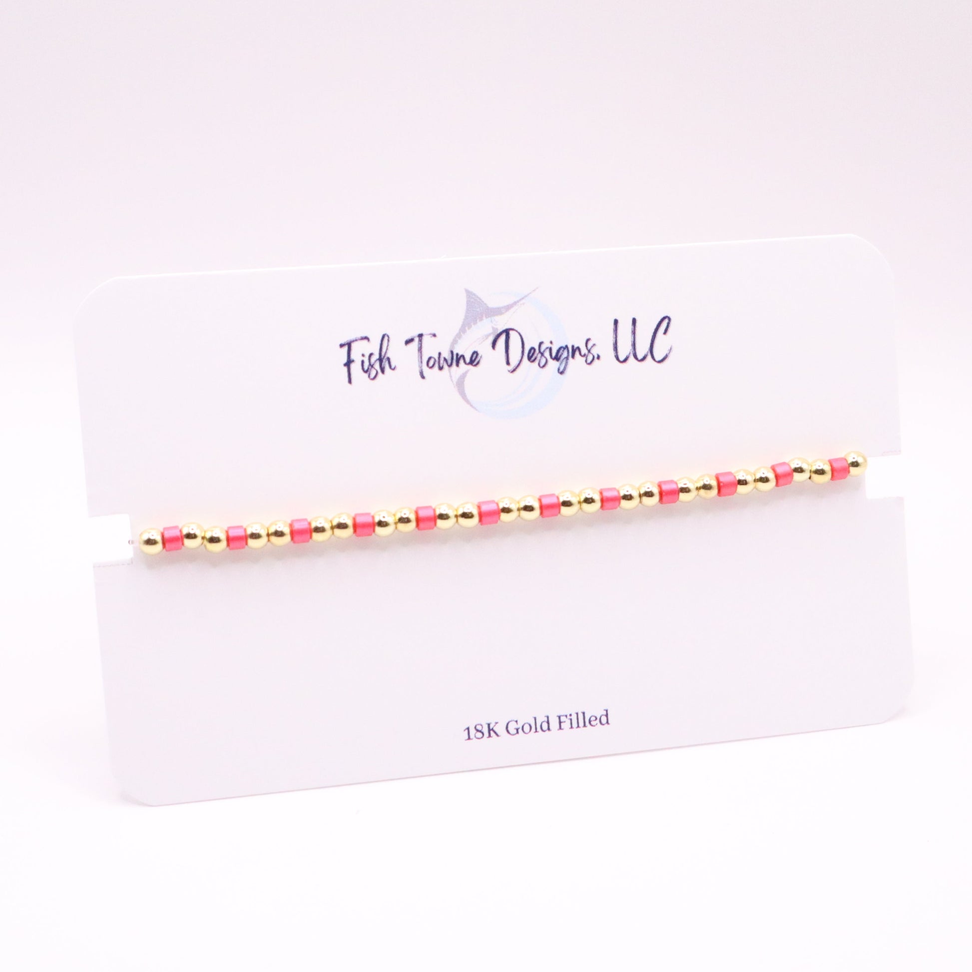 Gold and pink beaded bracelet on a white card with 'Fish Towne Designs, LLC' branding.