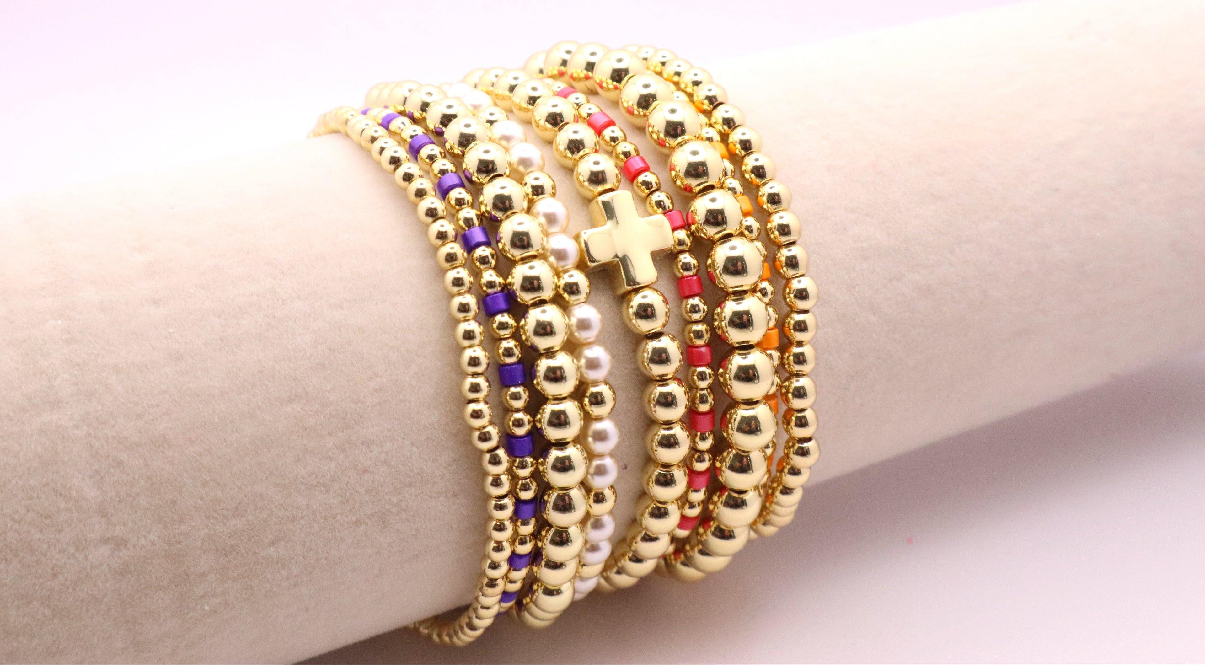 Gold beaded bracelets on a wrist against a light background
