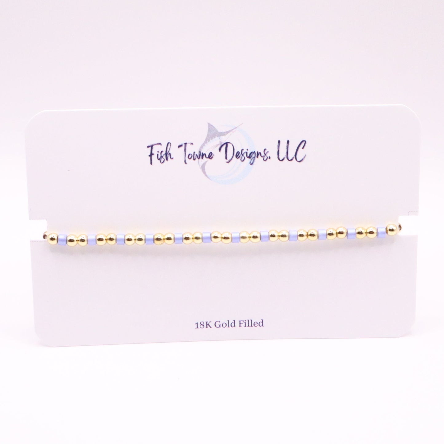 Gold and lilac beaded bracelet on a white card with 'Fish Towne Designs, LLC' branding.