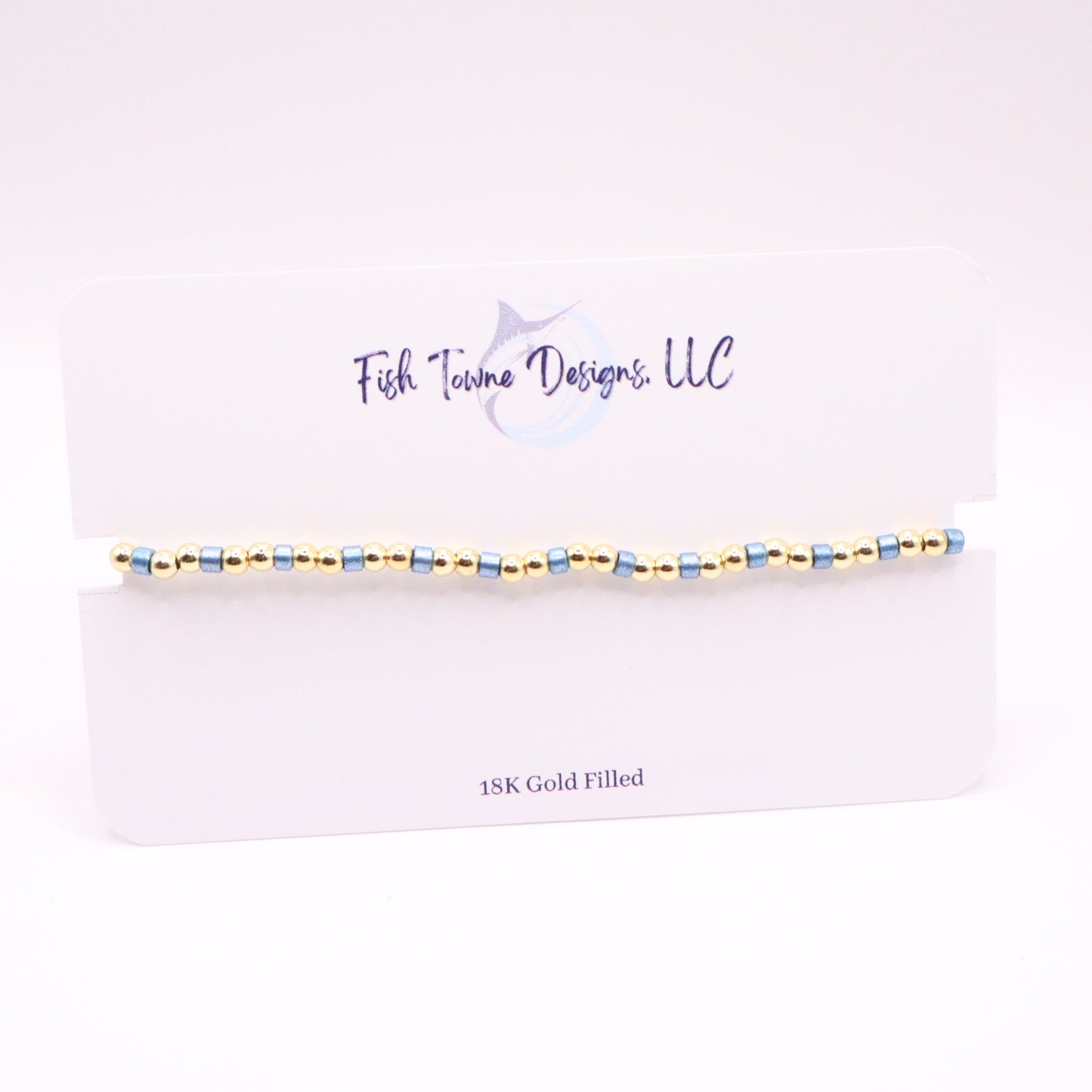 Gold and blue beaded bracelet on a white card with 'Fish Towne Designs, LLC' branding.
