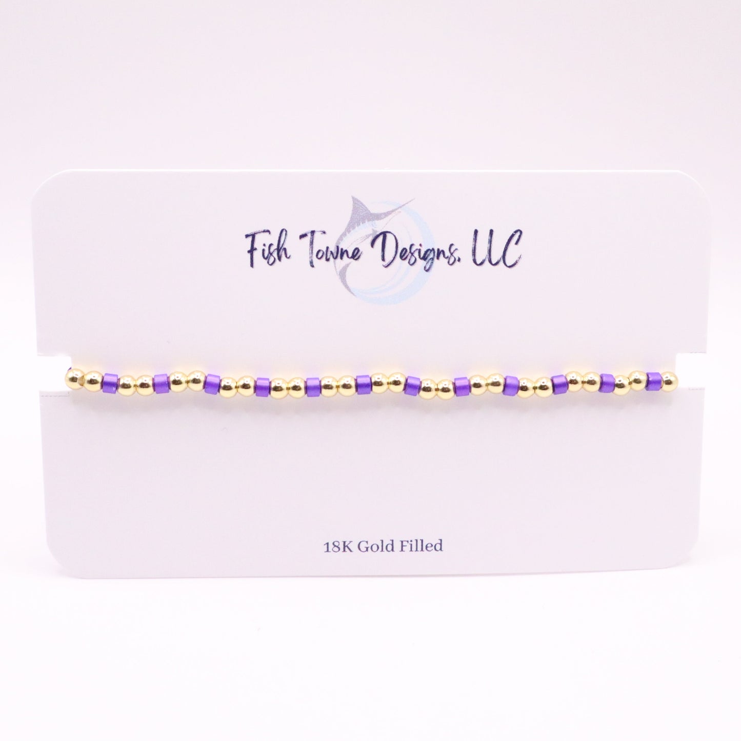 Bracelet with gold and purple beads on a white card with 'Fish Towne Designs, LLC' branding.