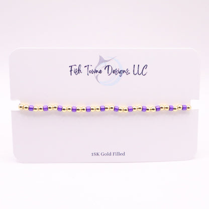 Bracelet with gold and purple beads on a white card with 'Fish Towne Designs, LLC' branding.