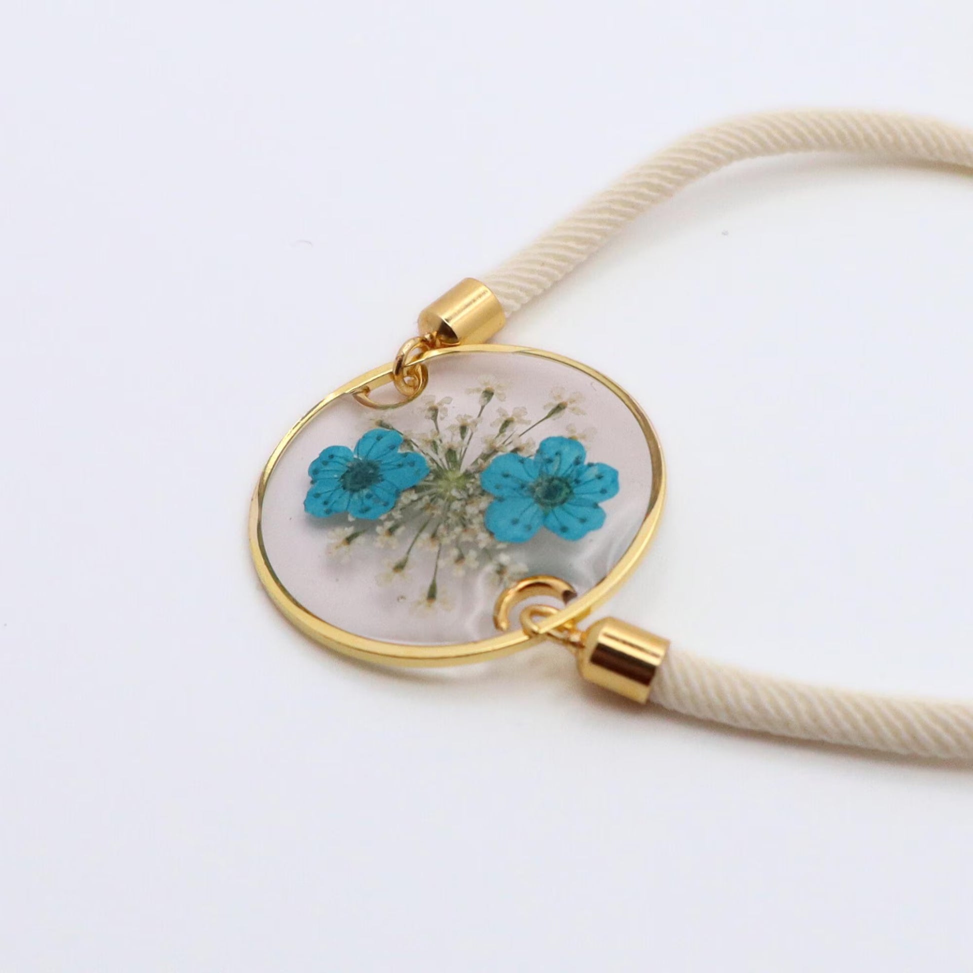 Handmade blue flower resin bracelet with gold round bezel and white adjustable cord on white background