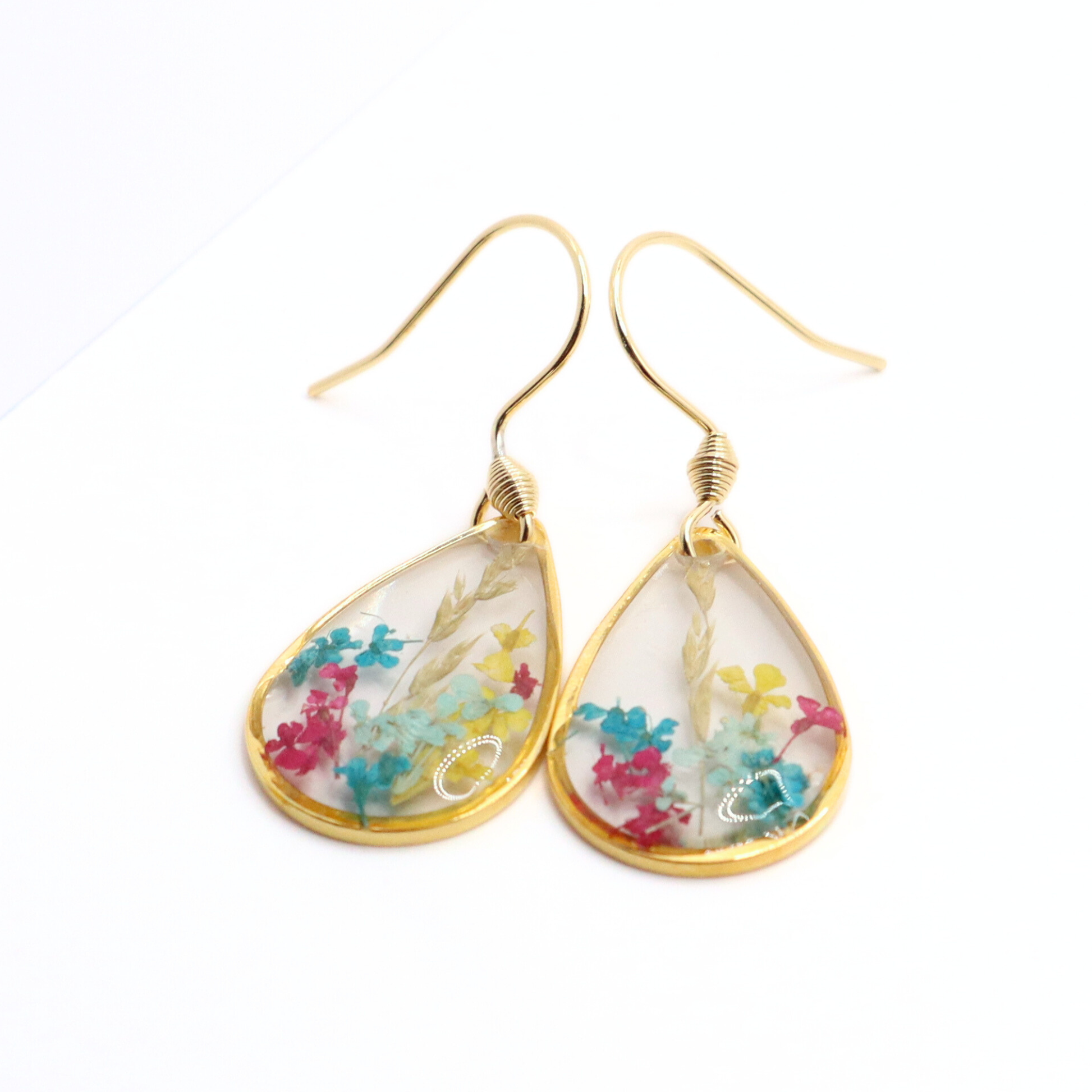 Close-up of gold teardrop earrings with preserved colorful flowers embedded in clear resin