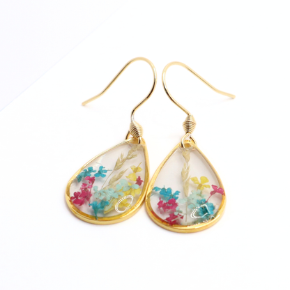 Close-up of gold teardrop earrings with preserved colorful flowers embedded in clear resin