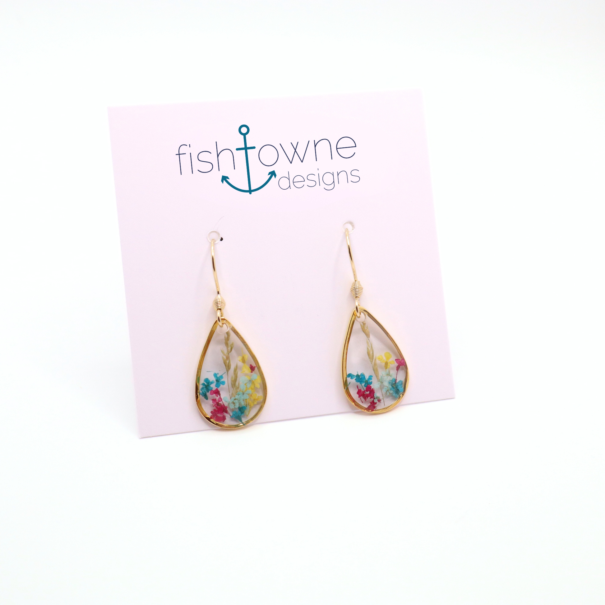 Teardrop resin earrings with real dried flowers in pink, blue, and yellow, set in gold frames on a display card