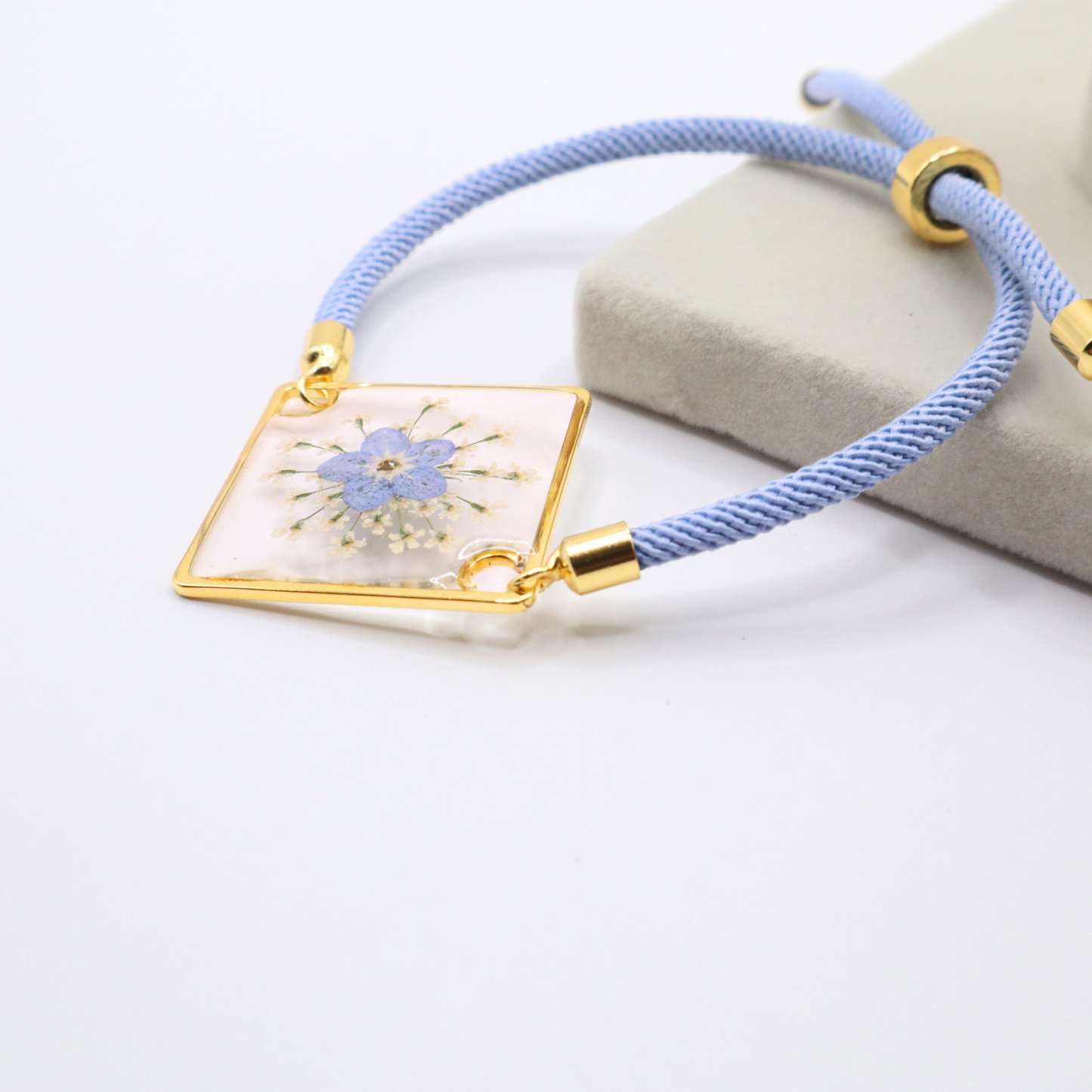 Top view blue forget-me-not flower resin bracelet with gold frame and adjustable cord minimalist jewelry