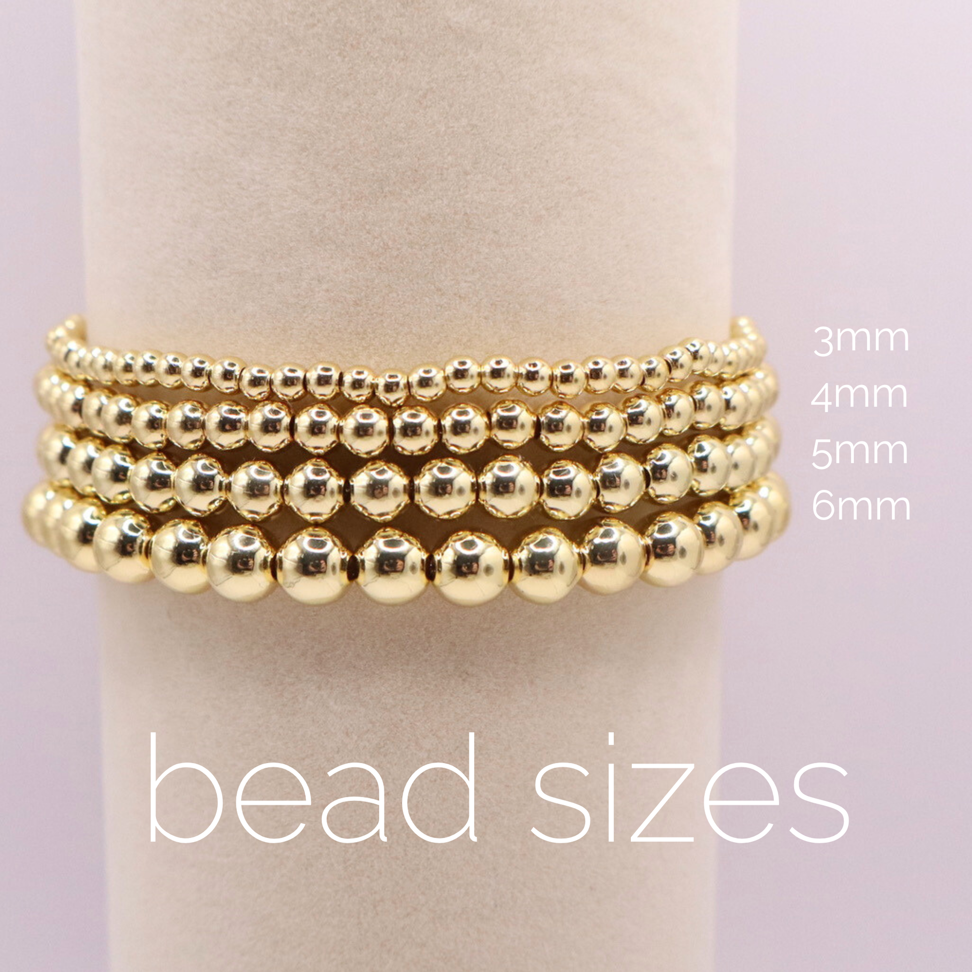 Close-up of four stacked 18K gold filled bead bracelets on a display stand, showcasing smooth polished finish and uniform design. The size of each bracket is noted: 3mm, 4mm, 5mm, and 6mm.