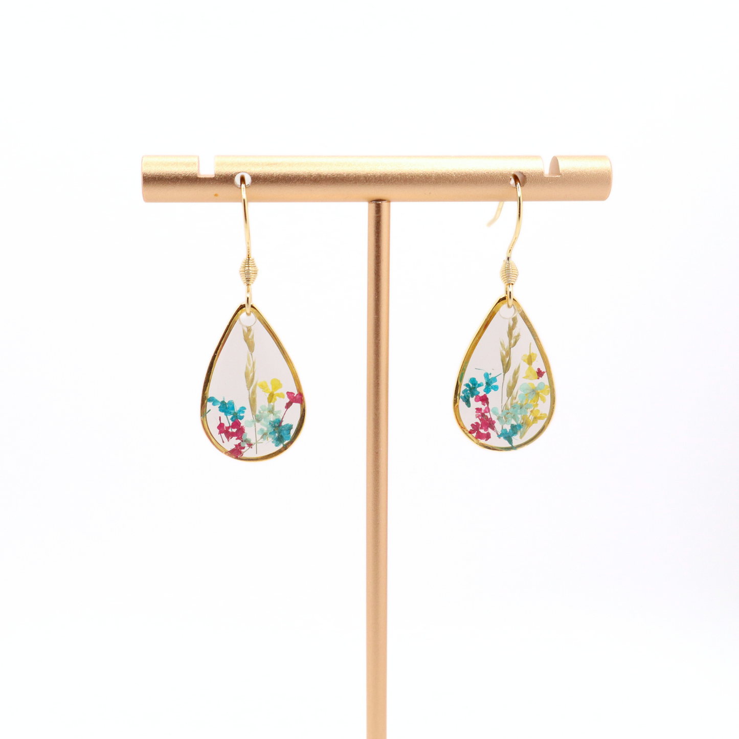 Handmade teardrop floral resin earrings with gold frames hanging on a gold stand against a white background