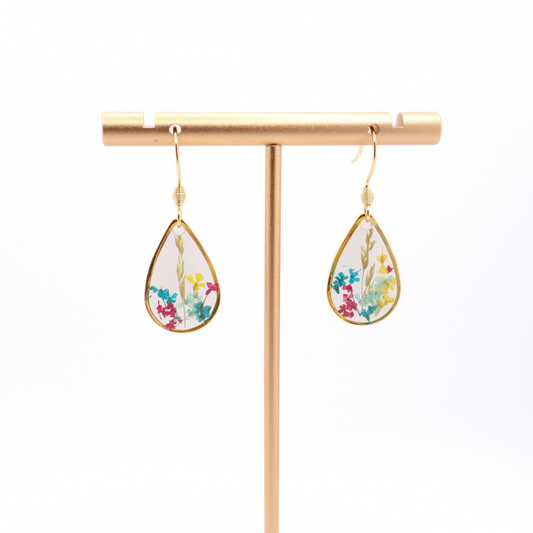 Handmade teardrop floral resin earrings with gold frames hanging on a gold stand against a white background