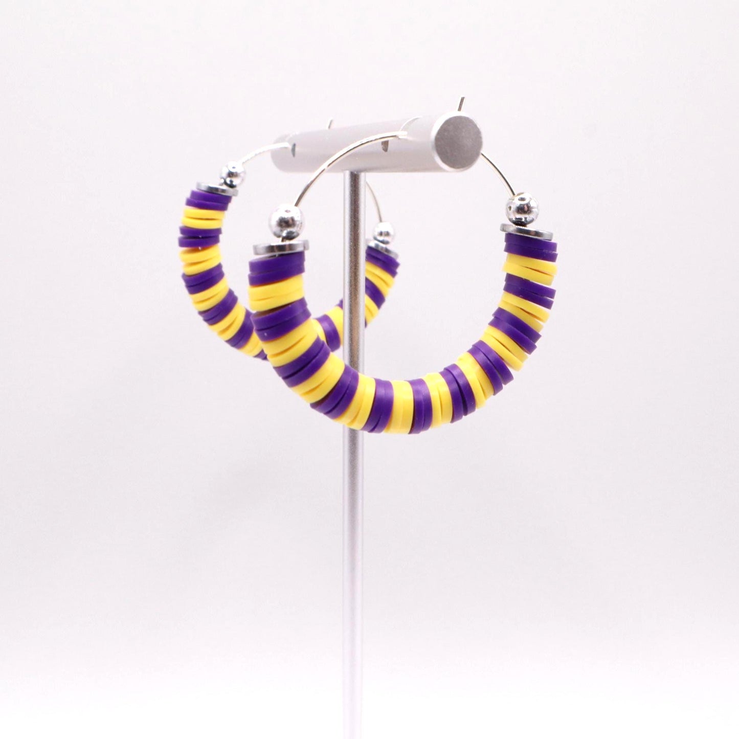 Close-up of purple and gold heishi bead hoop earrings with gold accents on a jewelry stand, highlighting bead detail and pattern