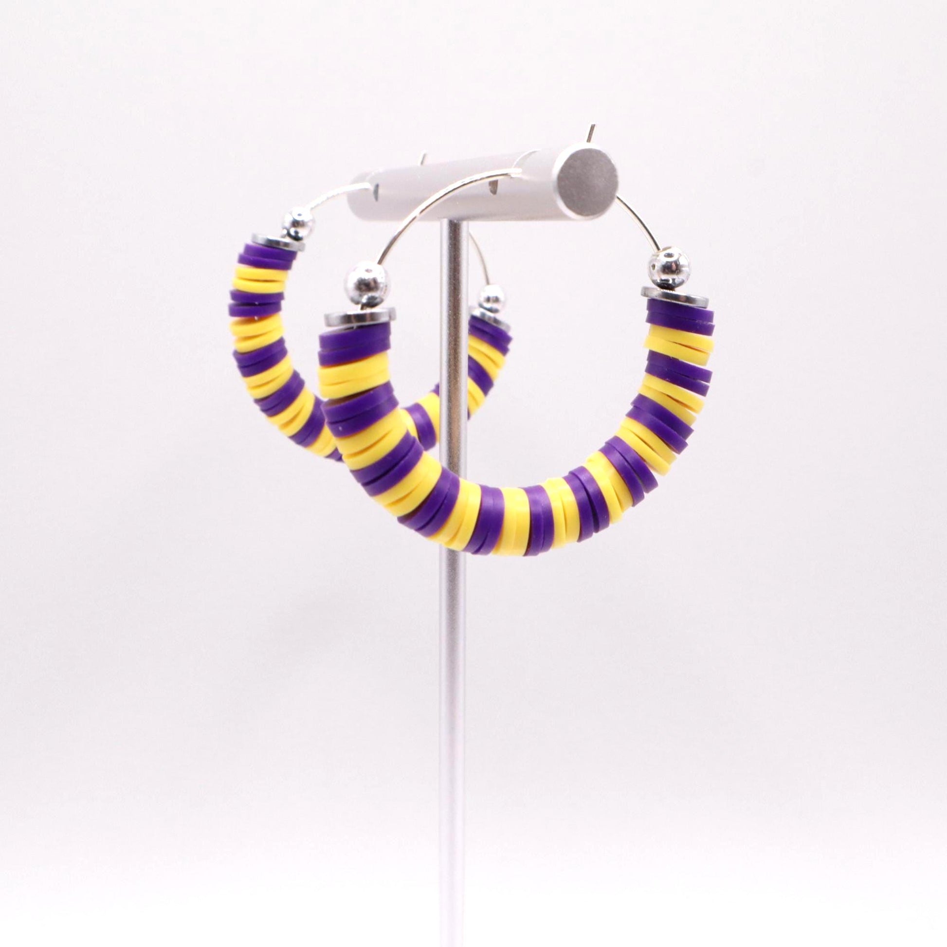 Close-up of purple and gold heishi bead hoop earrings with gold accents on a jewelry stand, highlighting bead detail and pattern