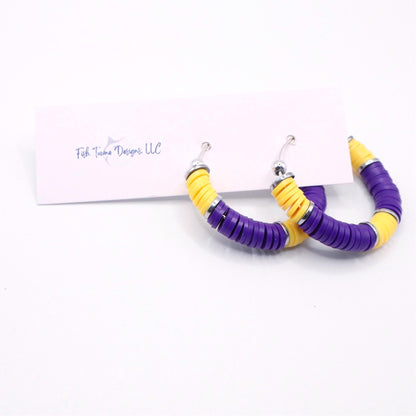 Purple and gold heishi bead hoop earrings with gold accents hanging on a minimalist jewelry stand against a white background