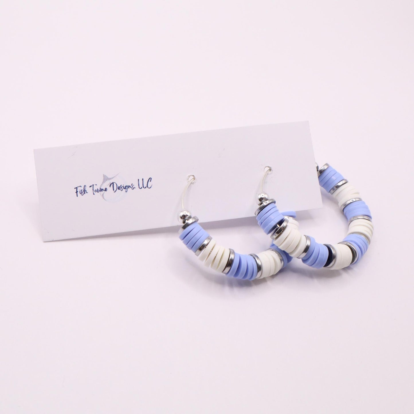 Handmade light blue and white polymer clay heishi bead hoop earrings with silver spacers shown on a white background with display card