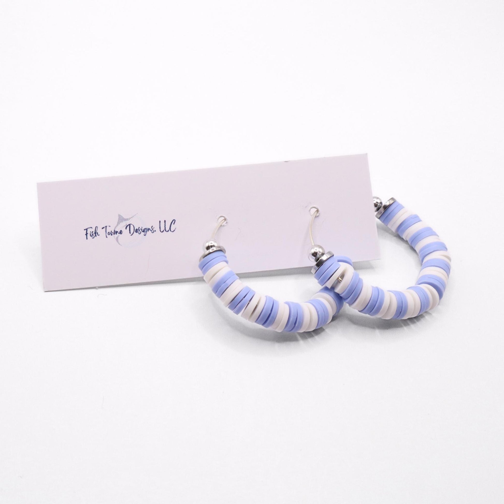 Light blue and white heishi bead hoop earrings with silver accents displayed on a branded card against a white background