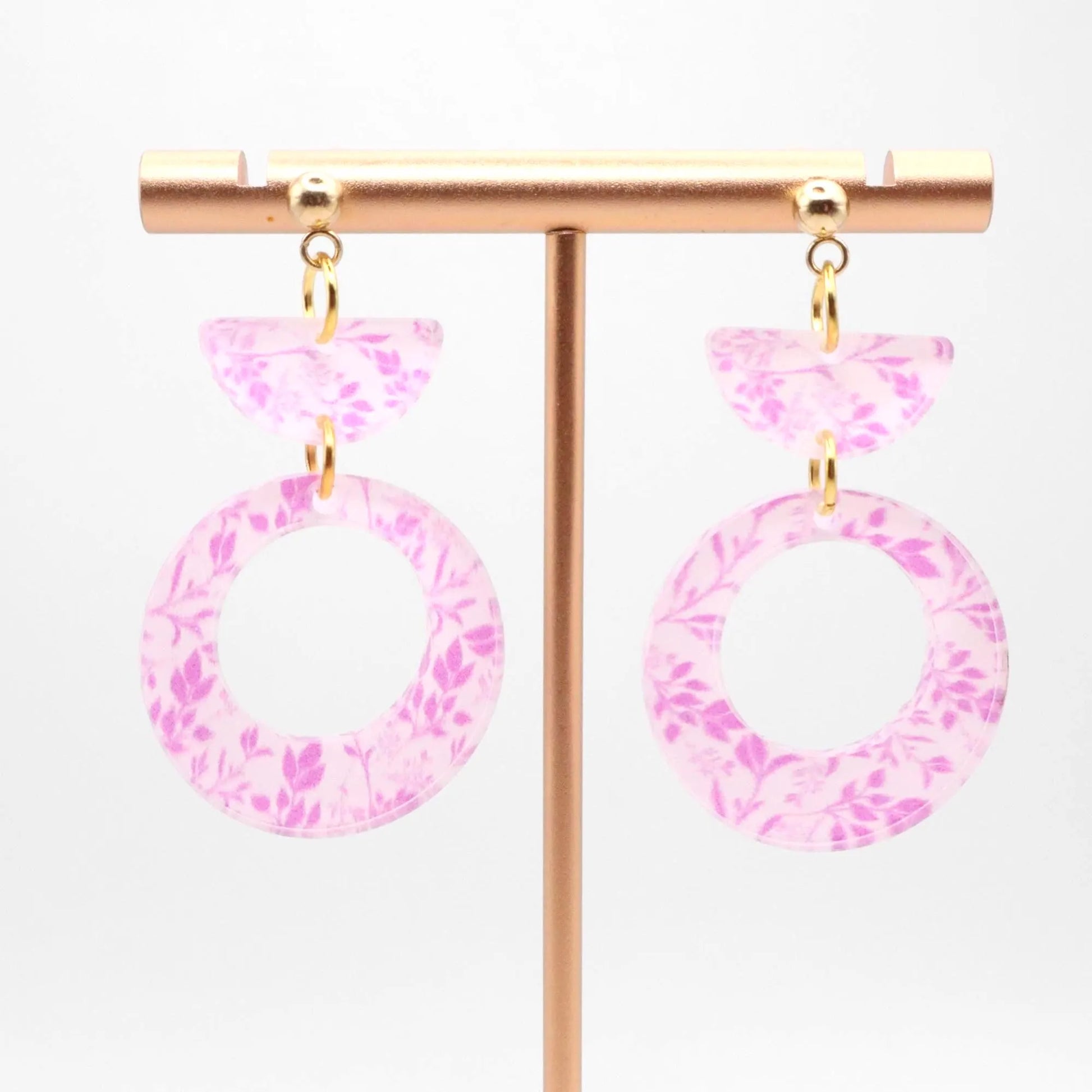 Pink floral earrings on a gold earring stand against a white background