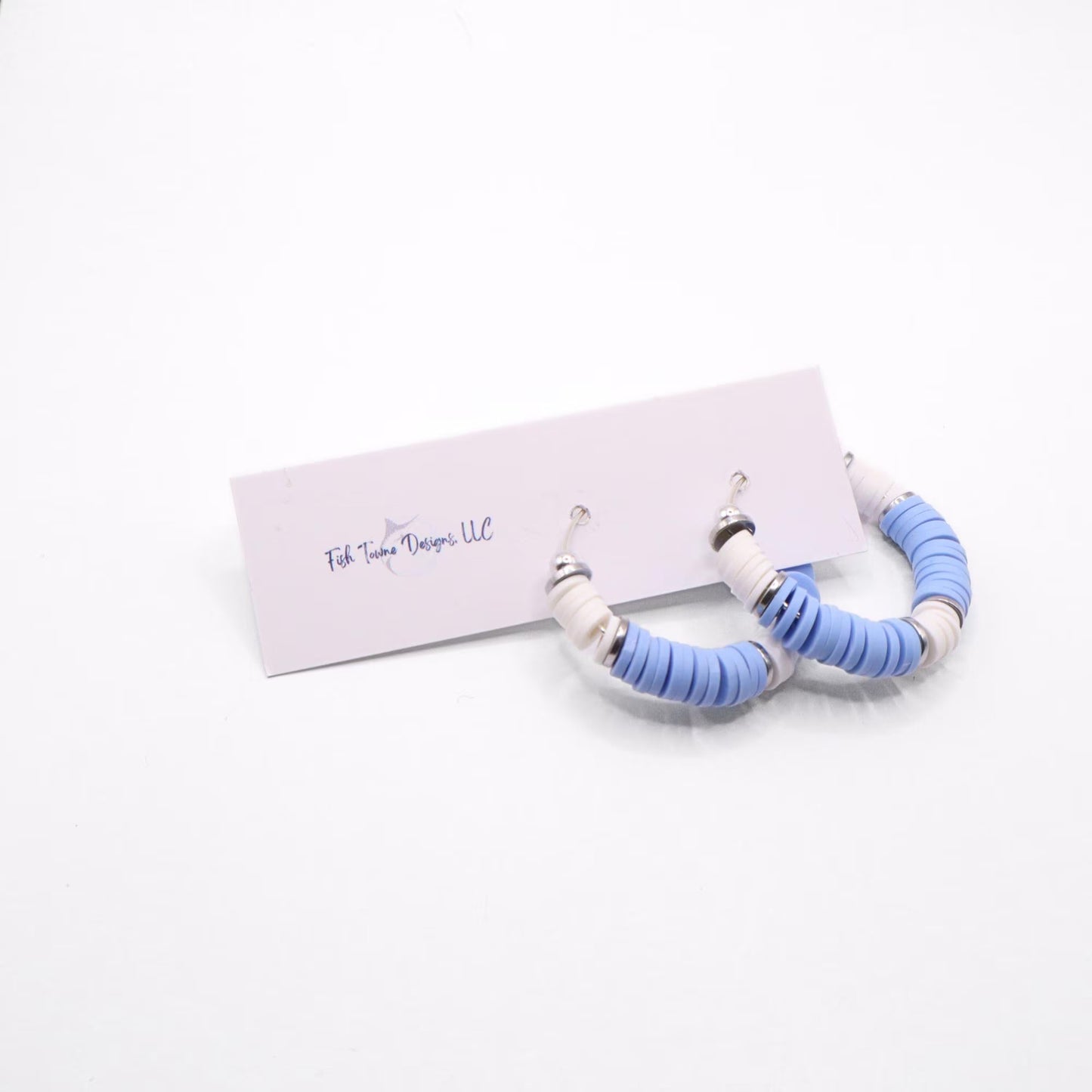 Light blue and white heishi bead hoop earrings with silver accents hanging on a minimalist jewelry stand against a white background
