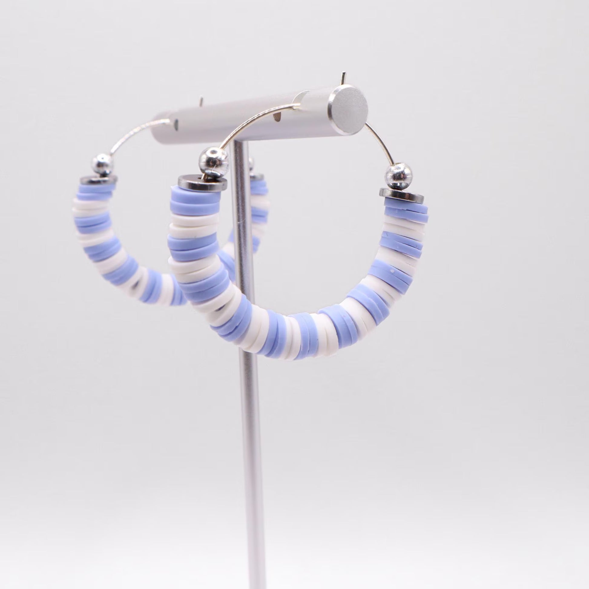 Close-up of light blue and white heishi bead hoop earrings with silver accents on a jewelry stand, highlighting bead detail and pattern