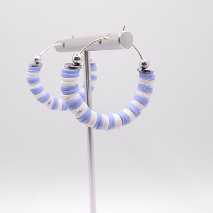 Close-up of light blue and white heishi bead hoop earrings with silver accents on a jewelry stand, highlighting bead detail and pattern