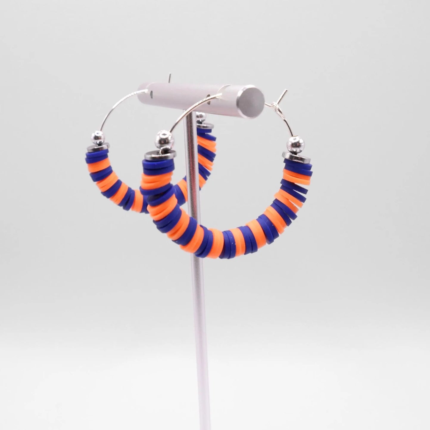 Close-up of blue and orange heishi bead hoop earrings with silver accents on a jewelry stand, highlighting bead detail and pattern