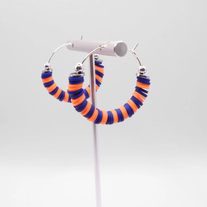 Close-up of blue and orange heishi bead hoop earrings with silver accents on a jewelry stand, highlighting bead detail and pattern