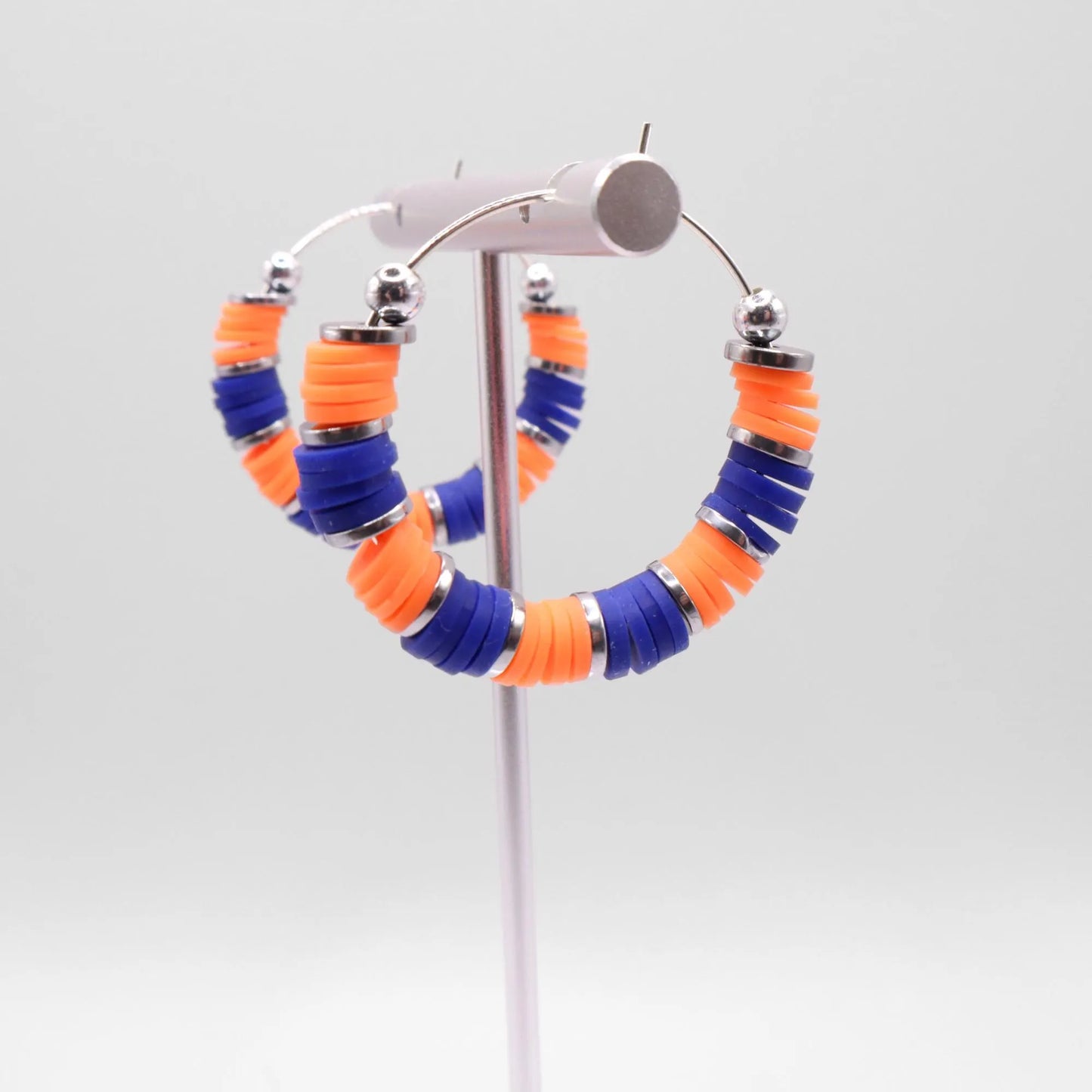 Blue and orange heishi bead hoop earrings with silver accents displayed on a branded card against a clean white background