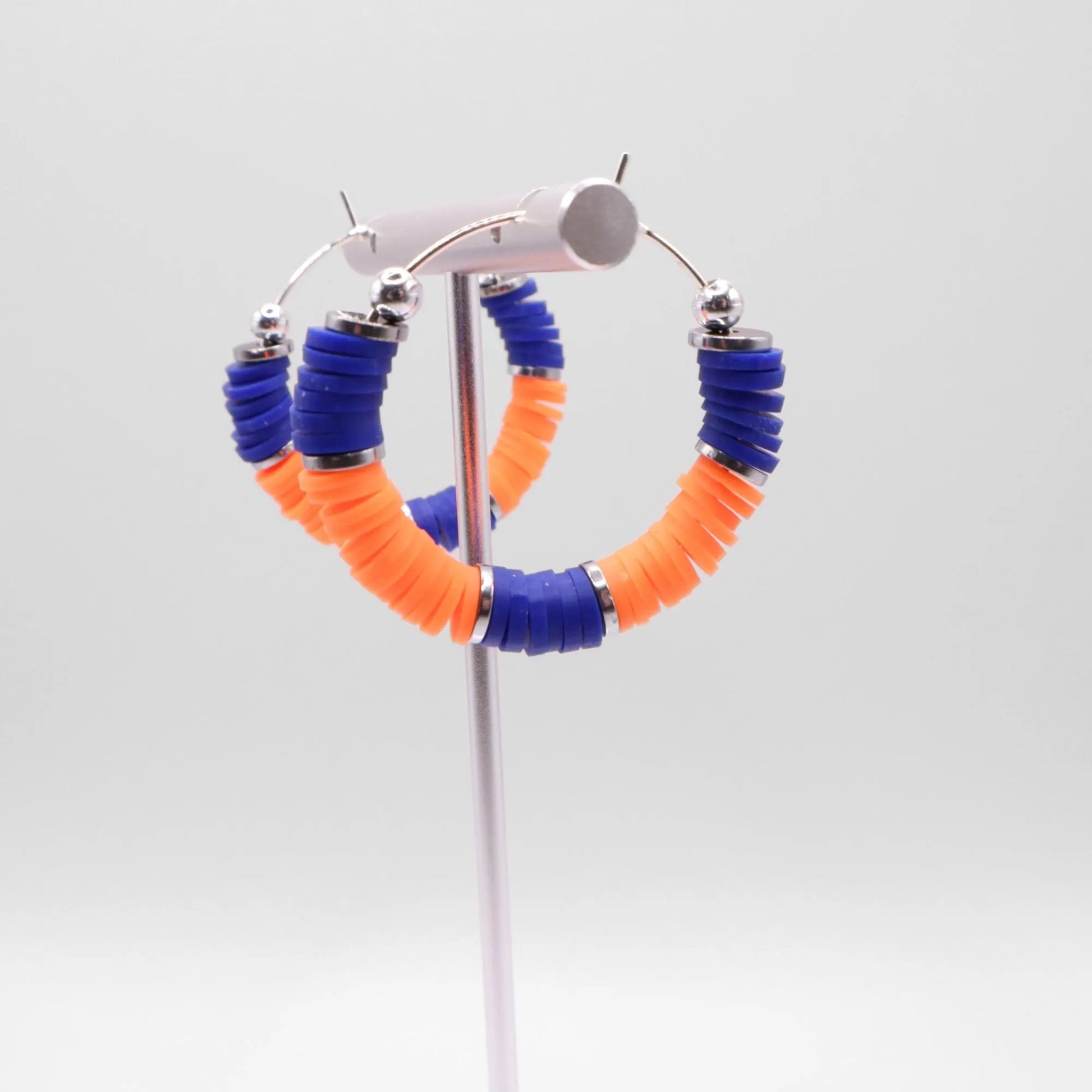 Side angle view of blue and orange heishi bead hoop earrings with silver spacers on a display stand against a white background
