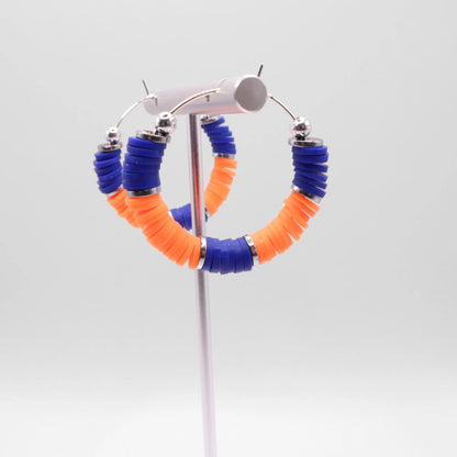 Side angle view of blue and orange heishi bead hoop earrings with silver spacers on a display stand against a white background