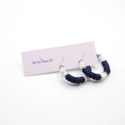Navy blue and white heishi bead hoop earrings with silver accents hanging on a minimalist jewelry stand against a white background