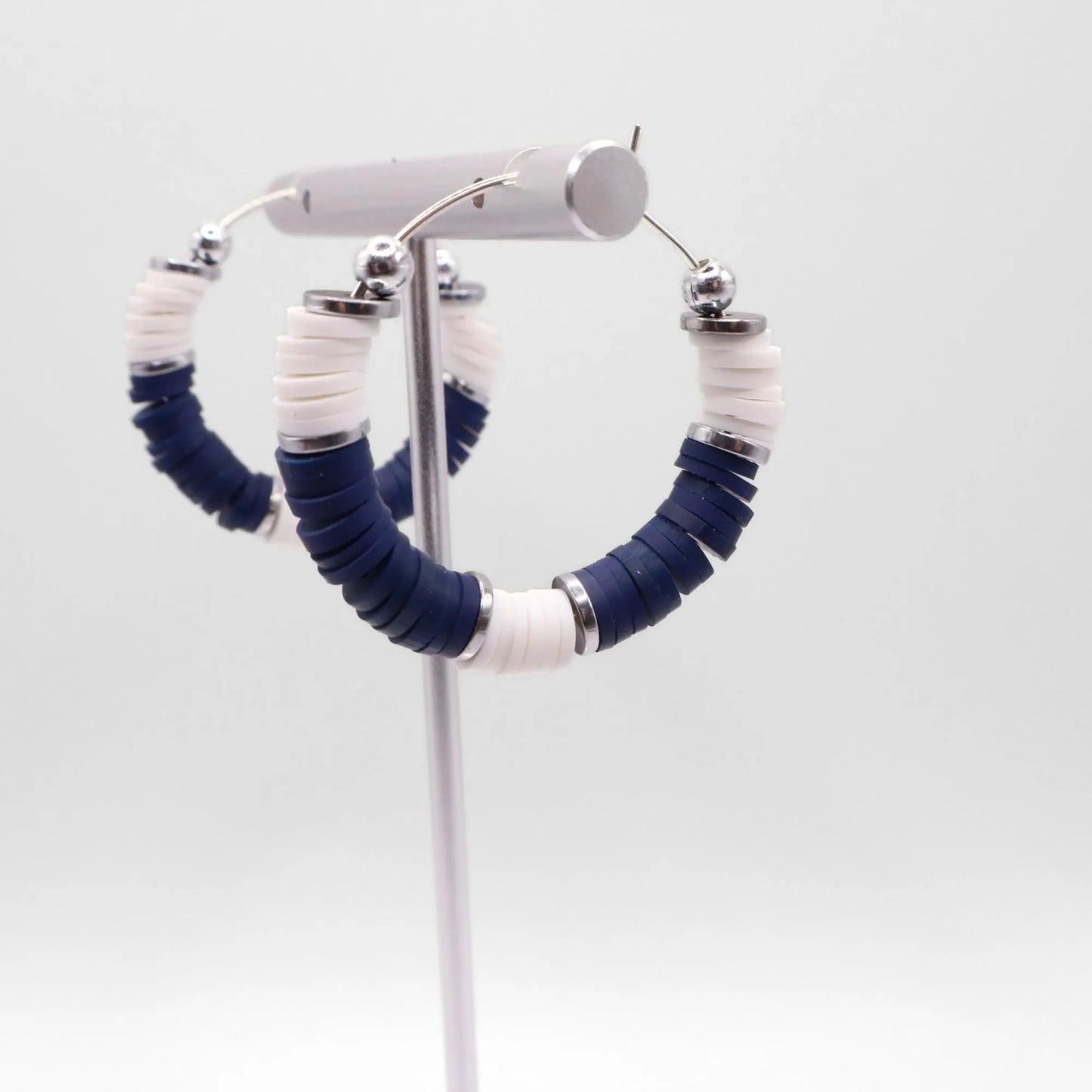 Side angle view of navy blue and white heishi bead hoop earrings with silver spacers on a display stand against a white background