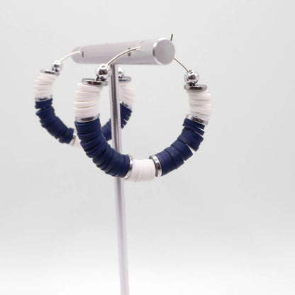 Side angle view of navy blue and white heishi bead hoop earrings with silver spacers on a display stand against a white background