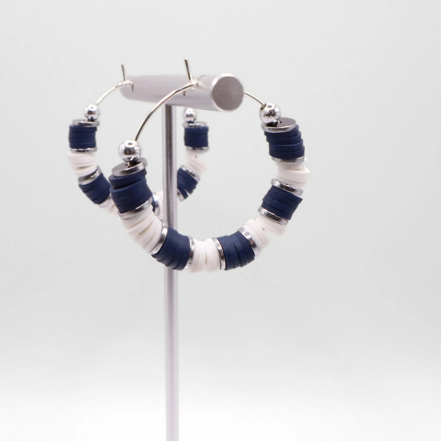 Close-up of navy blue and white heishi bead hoop earrings with silver accents on a jewelry stand, highlighting bead detail and pattern