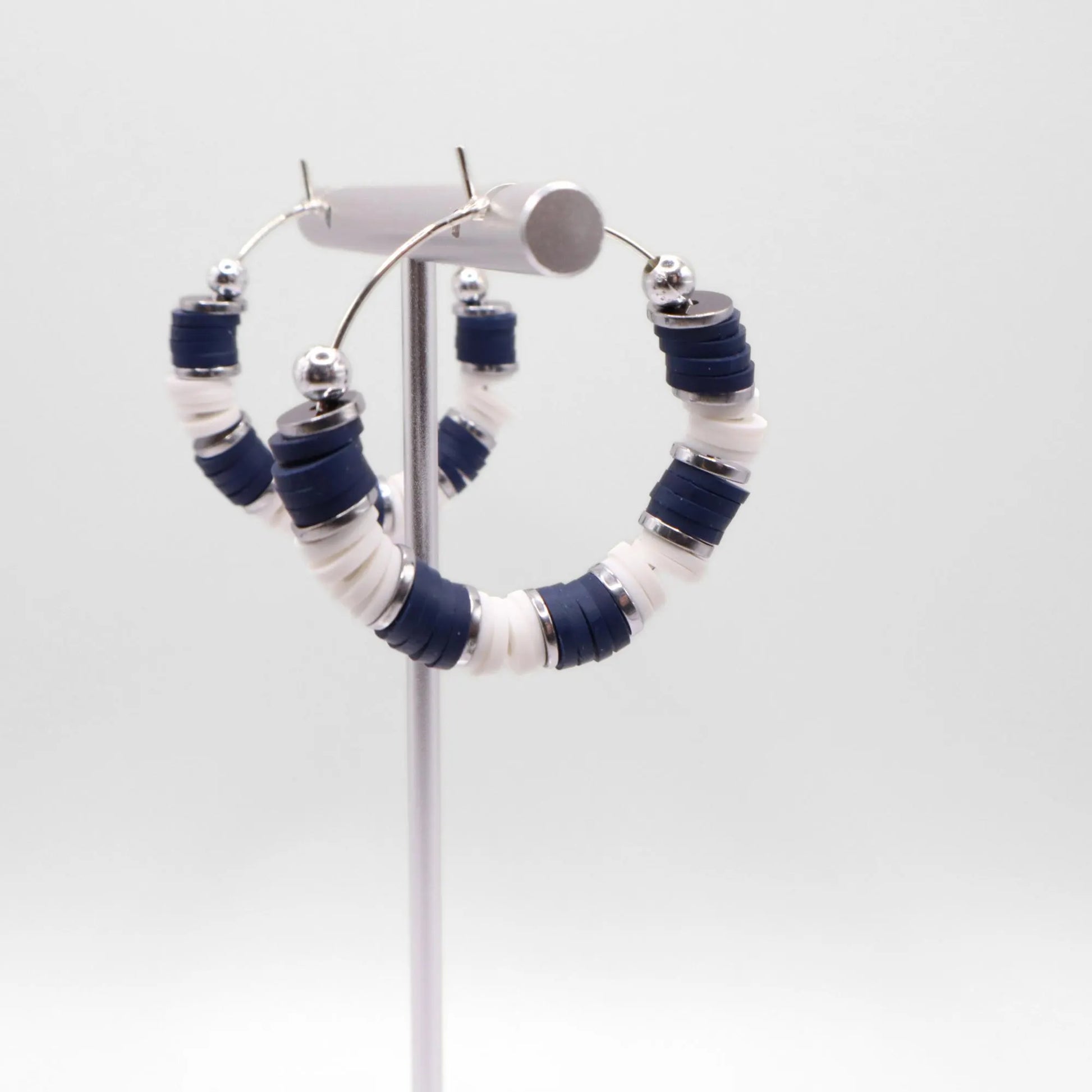 Close-up of navy blue and white heishi bead hoop earrings with silver accents on a jewelry stand, highlighting bead detail and pattern