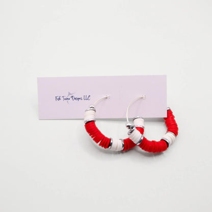 Red and white heishi bead hoop earrings with silver accents hanging on a minimalist jewelry stand against a white background