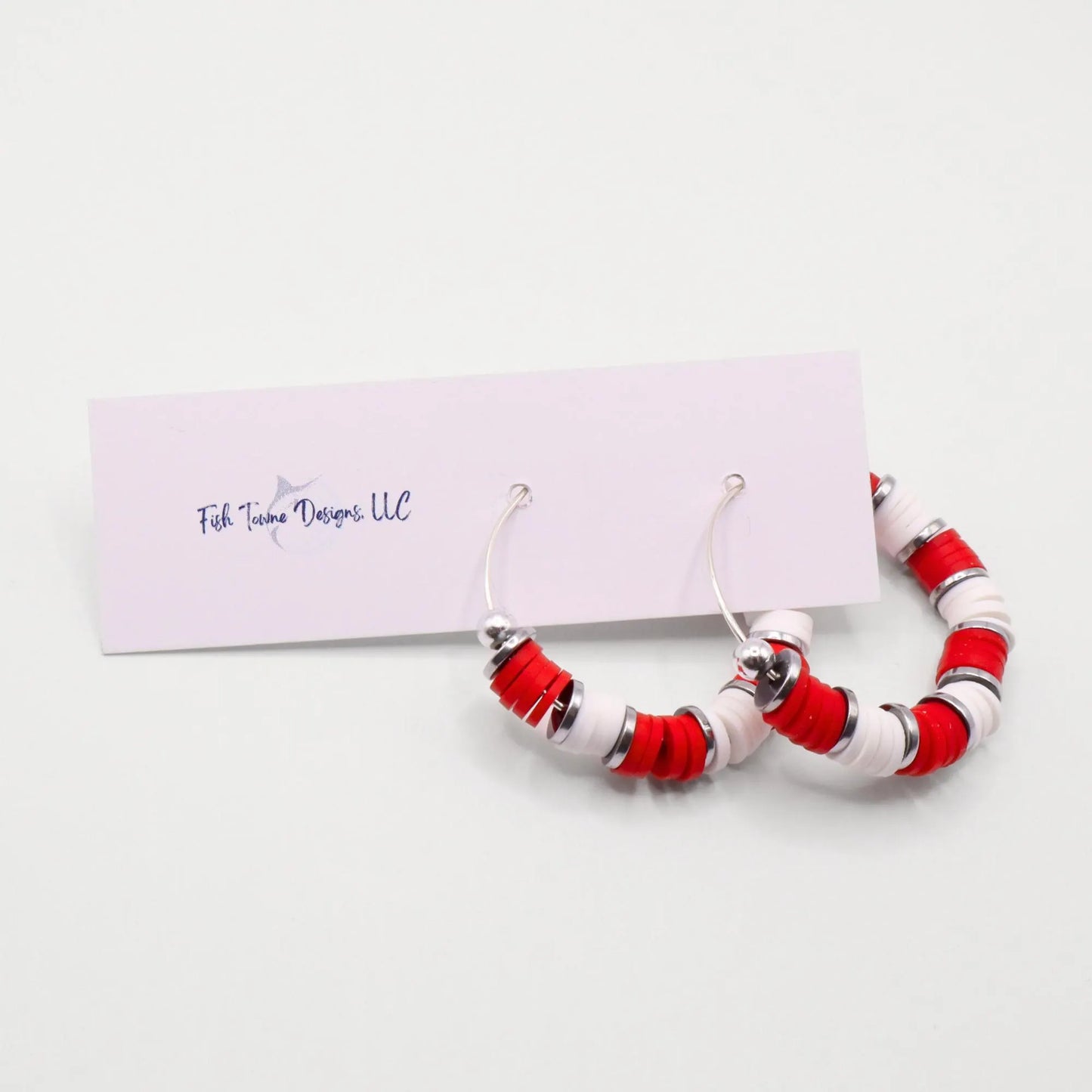 Handmade red and white polymer clay heishi bead hoop earrings with silver spacers shown on a white background with display card