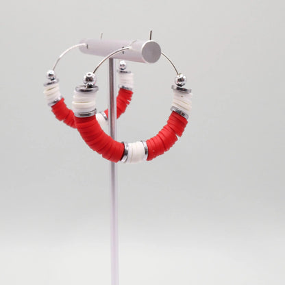 Close-up of red and white heishi bead hoop earrings with silver accents on a jewelry stand, highlighting bead detail and pattern