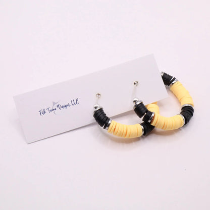Black and yellow heishi bead hoop earrings with silver accents hanging on a minimalist jewelry stand against a white background