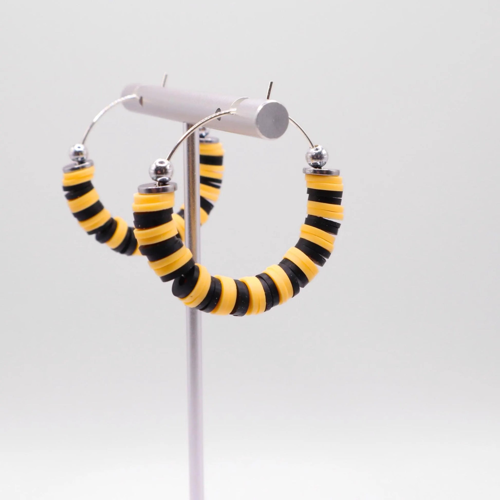 Side angle view of black and yellow heishi bead hoop earrings with silver spacers on a display stand against a white background