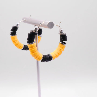 Close-up of black and yellow heishi bead hoop earrings with silver accents on a jewelry stand, highlighting bead detail and pattern