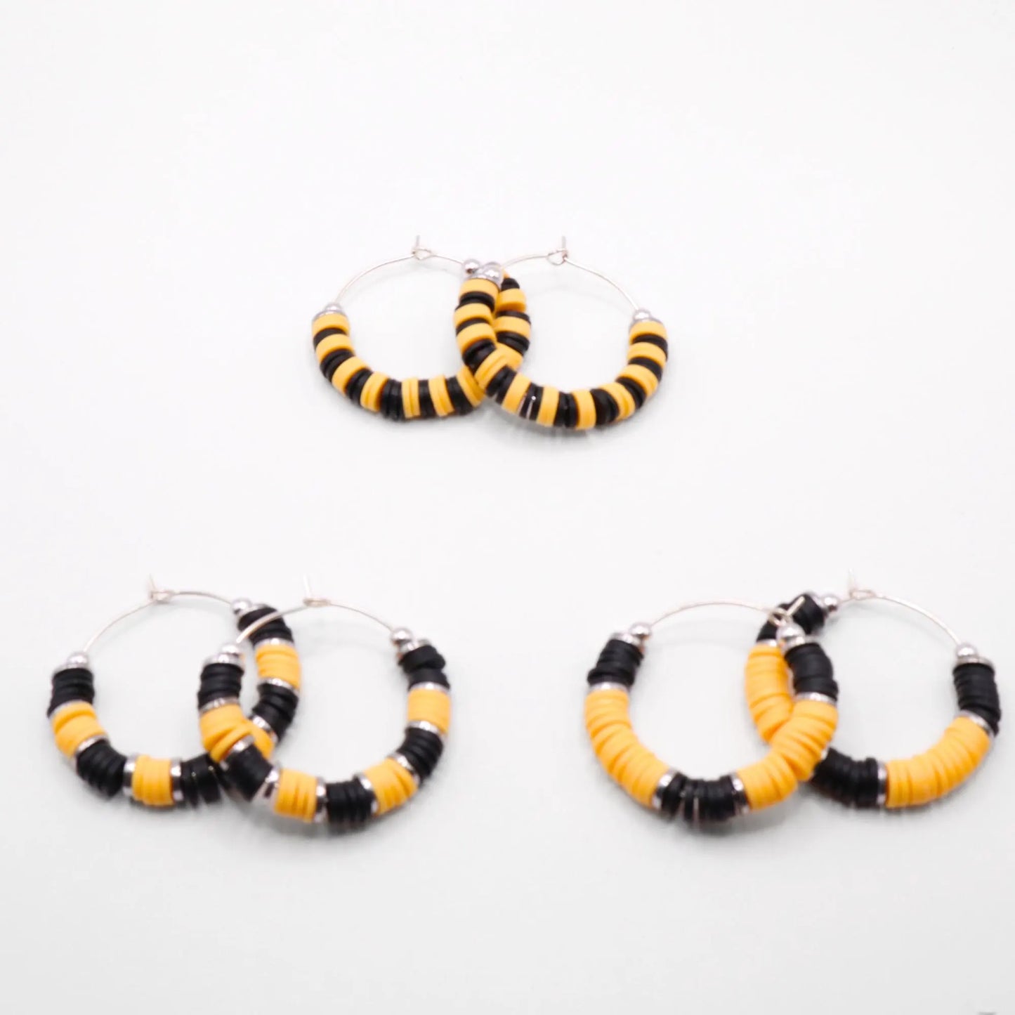 Set of three black and yellow heishi bead hoop earring styles arranged on a white background, showcasing size and pattern variations