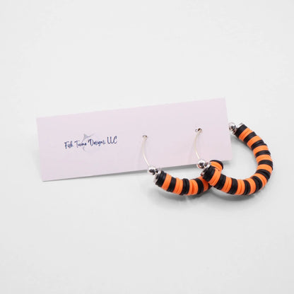 Orange and black heishi bead hoop earrings with silver accents displayed on a branded card against a white background