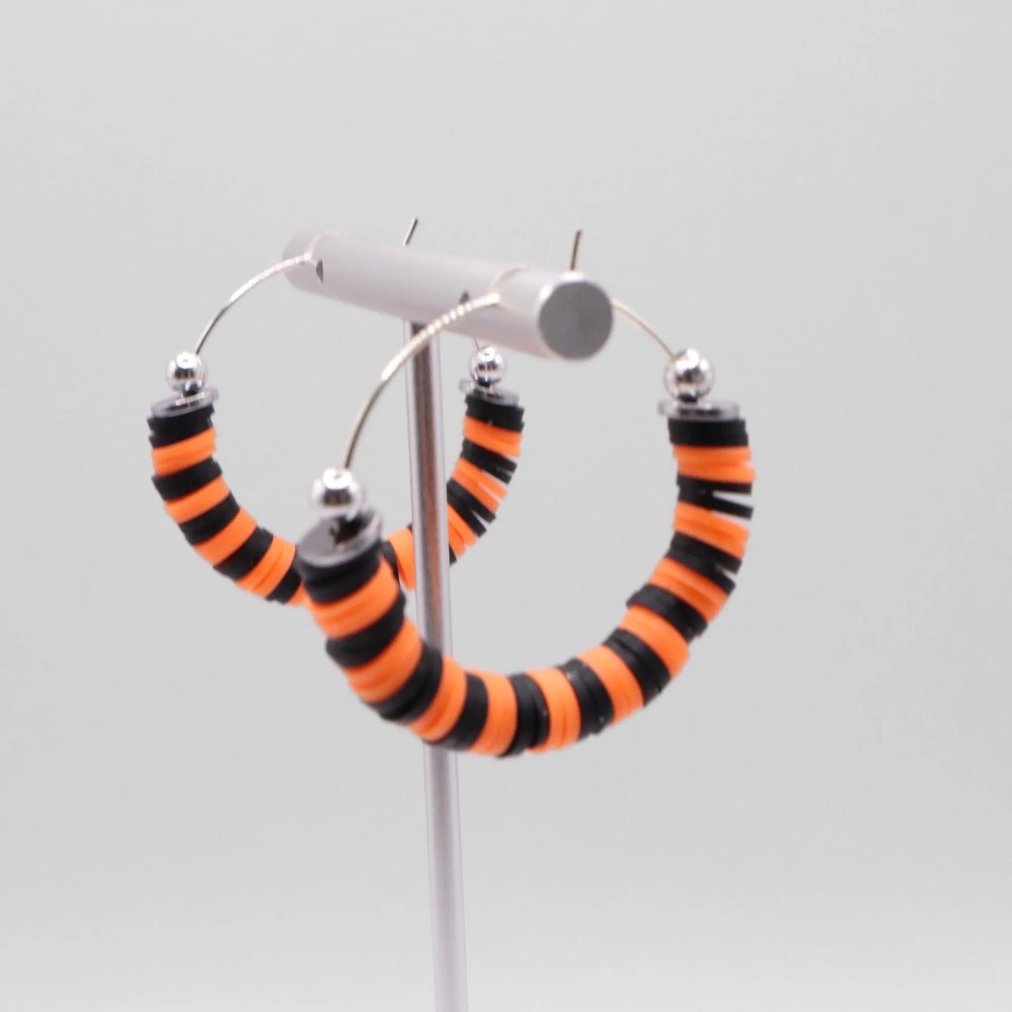 Handmade orange and black polymer clay heishi bead hoop earrings with silver spacers shown on a white background with display card