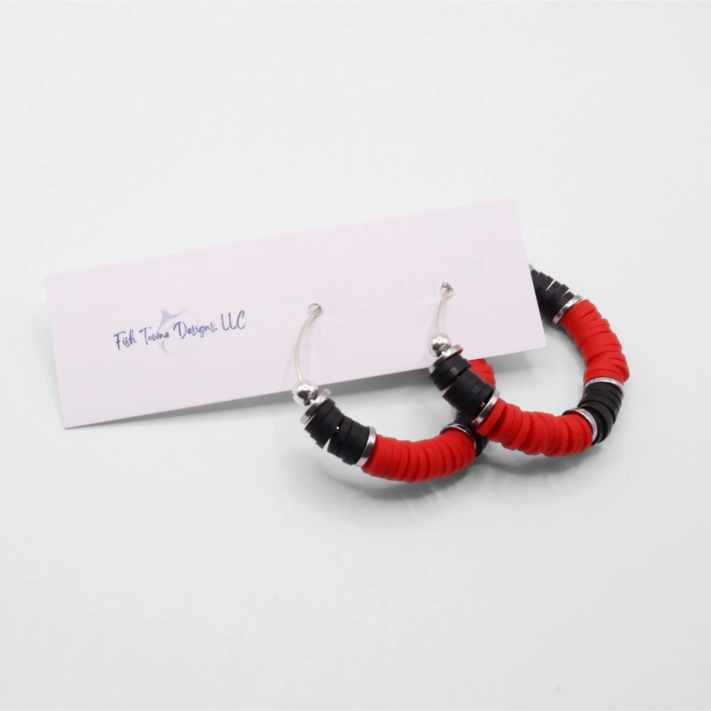 Side angle view of red and black heishi bead hoop earrings with silver spacers on a display stand against a white background