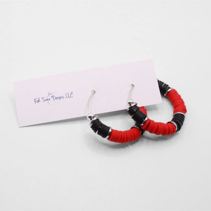 Side angle view of red and black heishi bead hoop earrings with silver spacers on a display stand against a white background