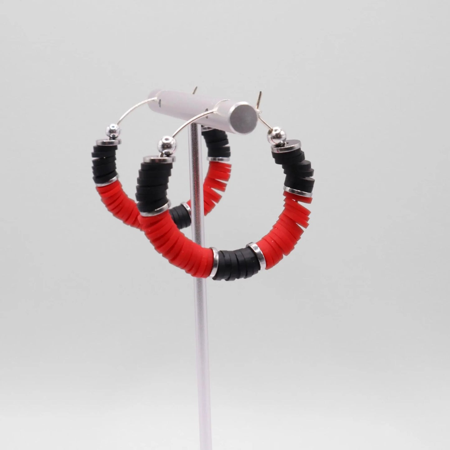 Handmade red and black polymer clay heishi bead hoop earrings with silver spacers shown on a white background with display card