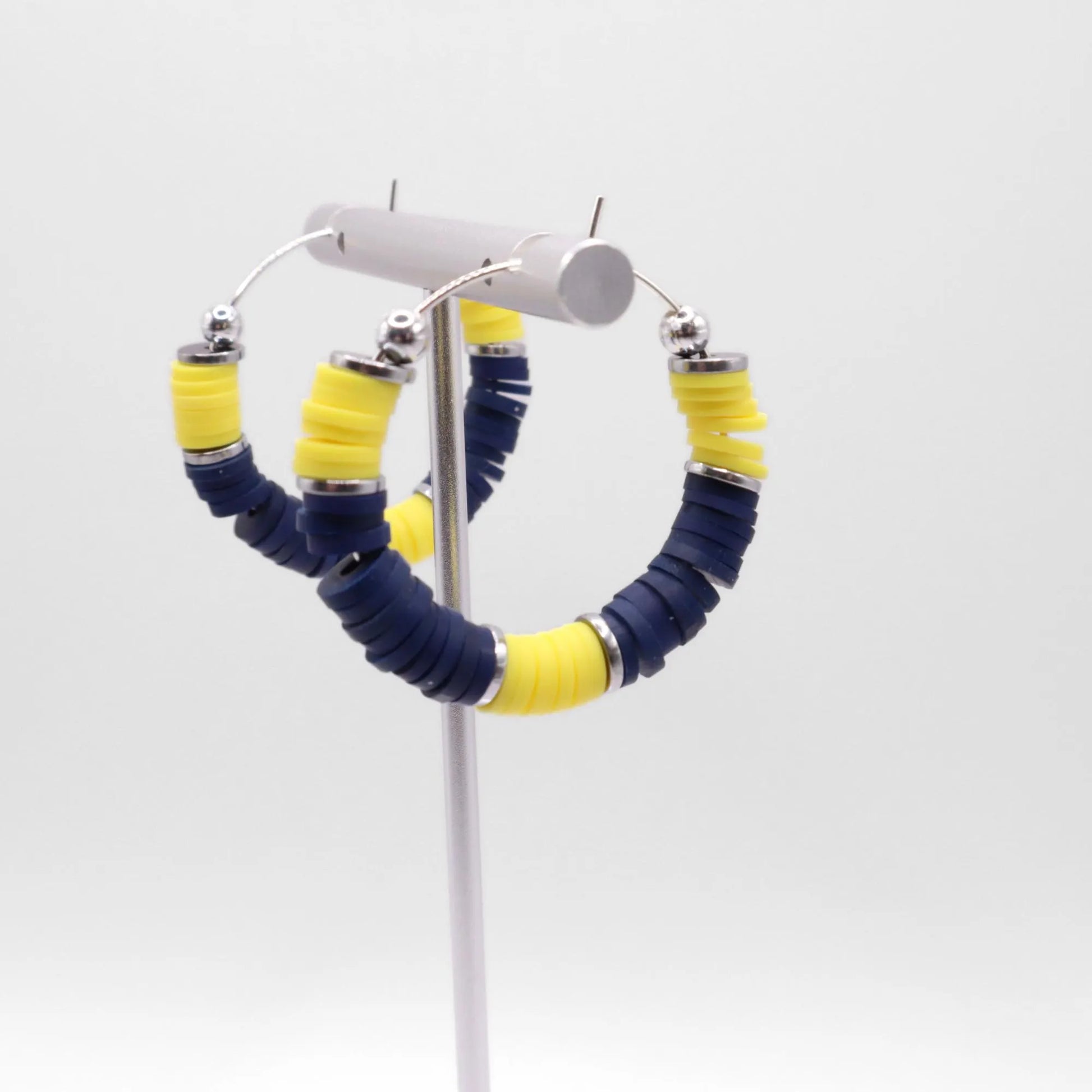 Close-up of navy blue and yellow heishi bead hoop earrings with silver accents on a jewelry stand, highlighting bead detail and pattern